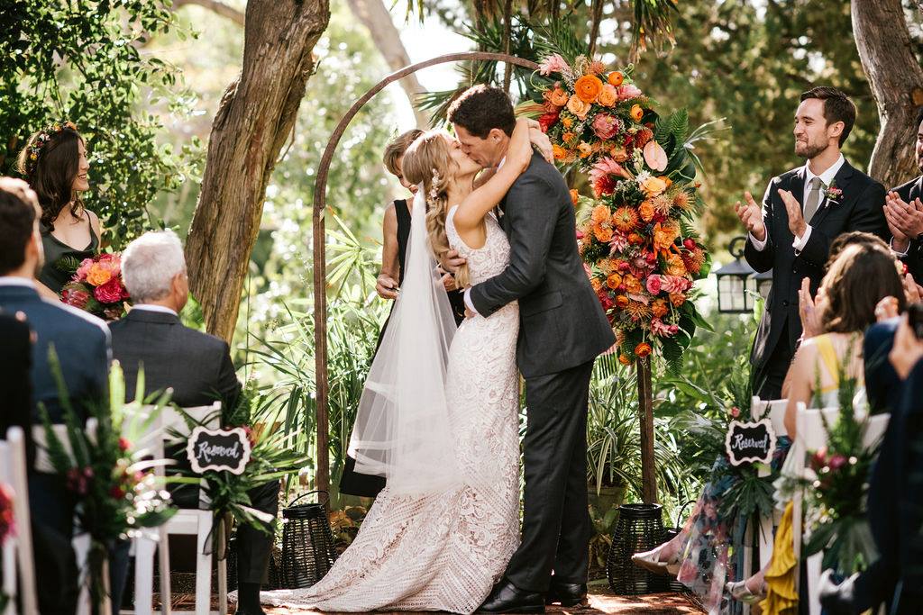 A bride and groom kissing in front of an arch.