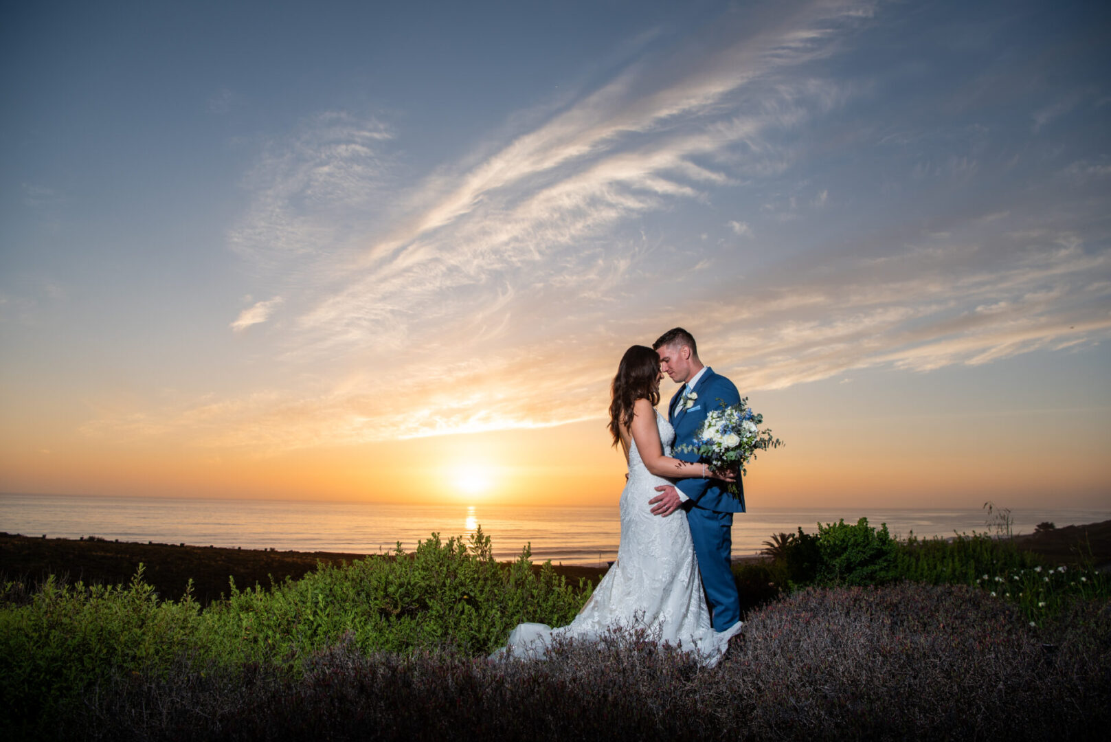 A bride and groom pose for the camera at sunset.