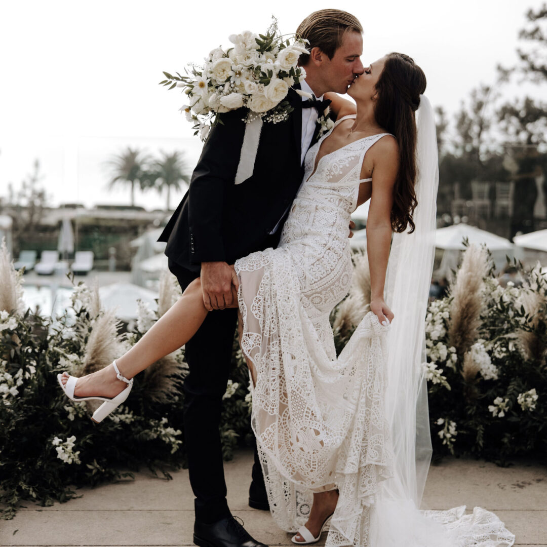 A man and woman kissing in front of some flowers.