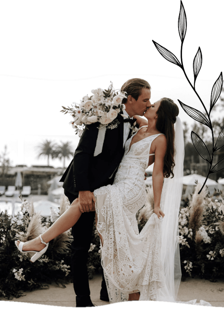 A man and woman kissing in front of some bushes.